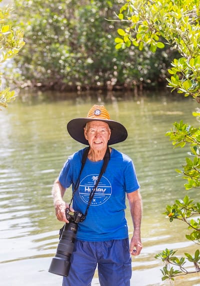 Older man standing by a waterway with a camera
