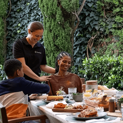 A caregiver assisting a resident at a meal outdoors.