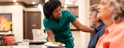 Staff member serving food to residents in a dining area