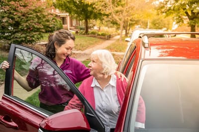 Caregiver assisting a senior into a vehicle outside
