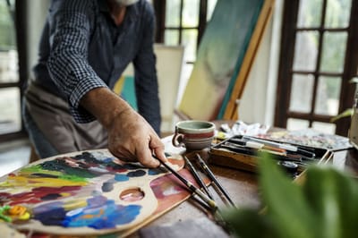 An older man painting in an art studio with various supplies