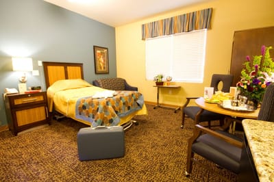 A cozy resident room with bed, seating area, and flowers