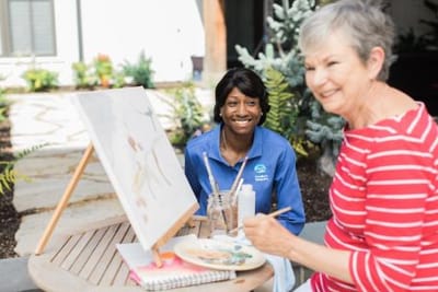 Residents painting outdoors with caregiver assistance