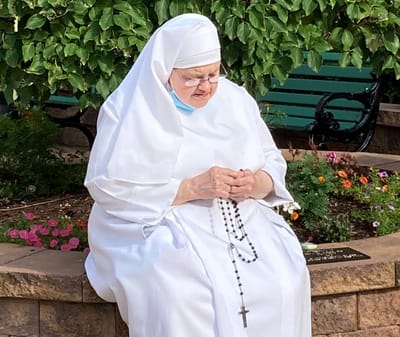 A nun praying in a garden area