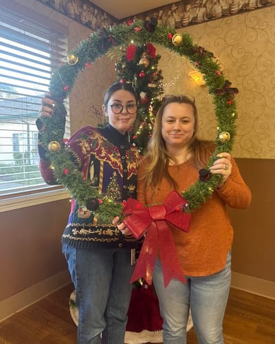 Two staff members posing with a holiday wreath