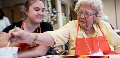 Senior resident painting with staff member in an activity room