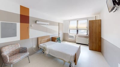 Bright interior of a resident room with a bed and chair