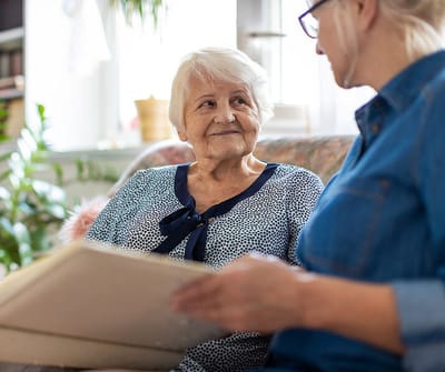 A senior woman smiles at a caregiver while looking at a photo album