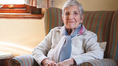 An elderly woman relaxing in a cozy chair inside the facility