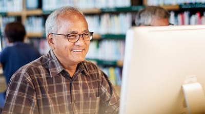 Senior man smiling while using a computer in a vibrant library