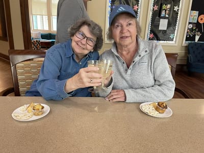 Two women toasting with drinks at a table.