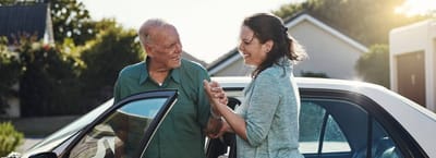 Senior man interacting with caregiver near a vehicle