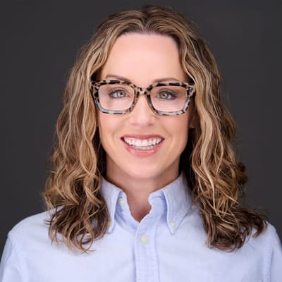 Smiling woman with glasses in front of a plain background.
