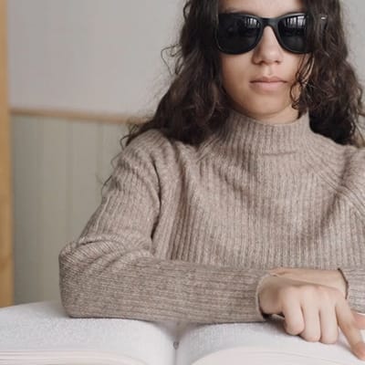 Young person wearing sunglasses reading a book.
