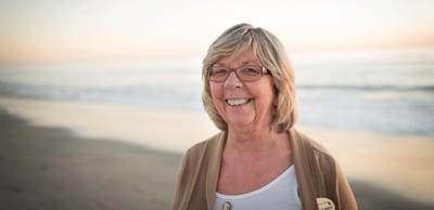 A smiling woman standing on the beach at sunset