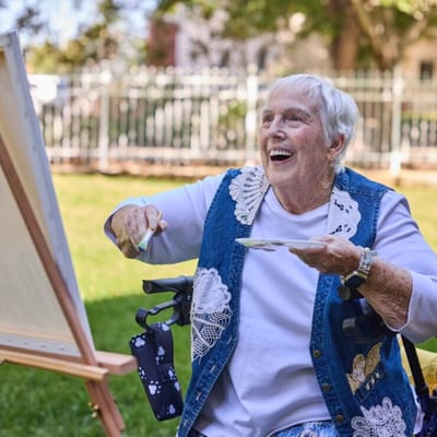 Elderly woman painting outdoors in a garden.
