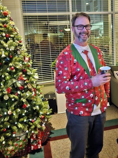 Staff member celebrating in holiday attire by a Christmas tree.