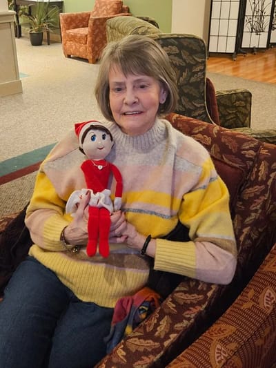 Resident holding a doll in a cozy lounge.