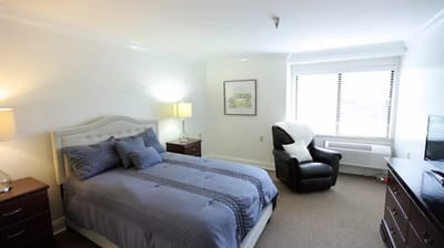 A well-furnished private resident room with a bed and chair
