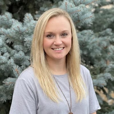 Smiling staff member posing in front of evergreen trees