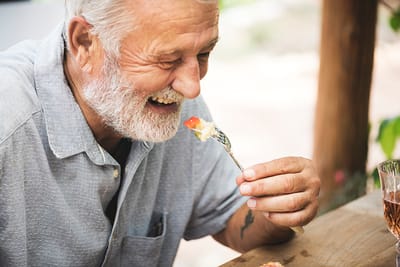 Smiling senior man enjoying food outdoors.