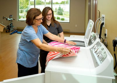 Senior resident and staff member doing laundry together.