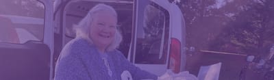 Senior woman smiling outdoors near a vehicle.