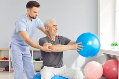 Therapist assisting senior with exercise ball