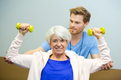 Older woman exercising with dumbbells and trainer.