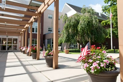Entryway of a senior living facility with flower pots and flags