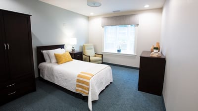Bright private resident room with a bed and chair