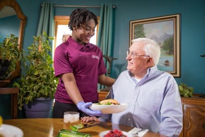 Staff member serving food to a senior resident in a dining setting