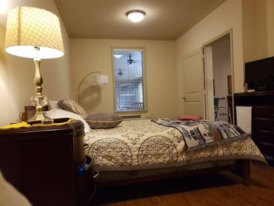 A cozy resident room with a neatly made bed and a lamp