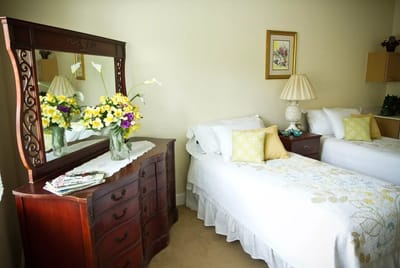 Cozy resident room with two beds and a beautifully arranged vanity.
