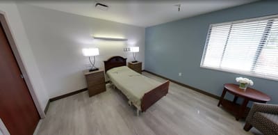 Brightly lit interior of a resident's room with a bed and side tables