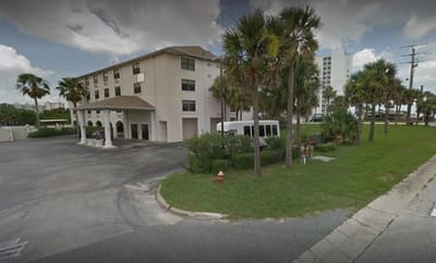 Exterior view of Seaside Manor with palm trees and a shuttle bus