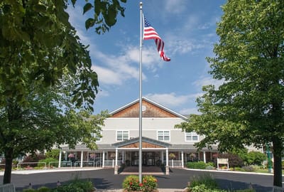 Front exterior of a senior living facility with trees and flag