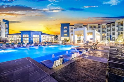 Outdoor pool area at sunset with seating and a building in view