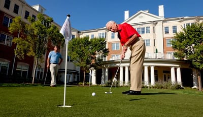 Elderly man putting golf ball on the lawn with a building in the background