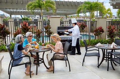 Residents enjoying a meal outdoors with a chef grilling