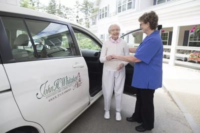 A resident being assisted by staff near a facility vehicle