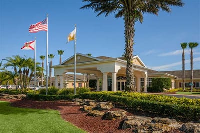Entrance of Life Care Center of Palm Bay with flags and palm trees