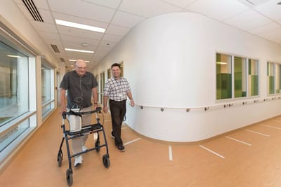 A senior resident walking with staff in a bright hallway