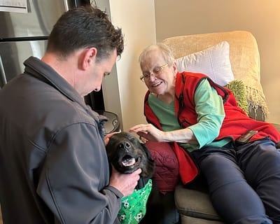 Elderly resident enjoying time with a therapy dog and staff member