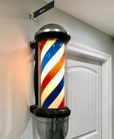 A brightly lit barber pole by a salon entrance