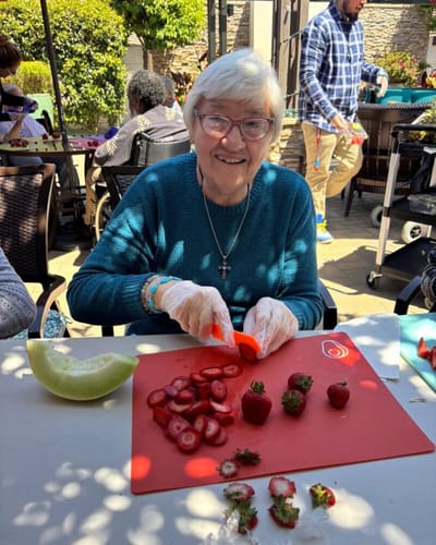 A resident preparing fruit outdoors with staff assistance