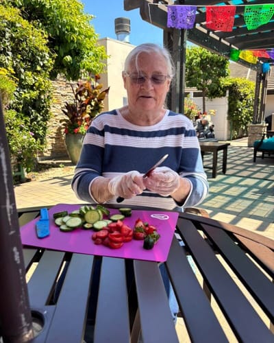 A resident preparing fruits outdoors at a vibrant facility.