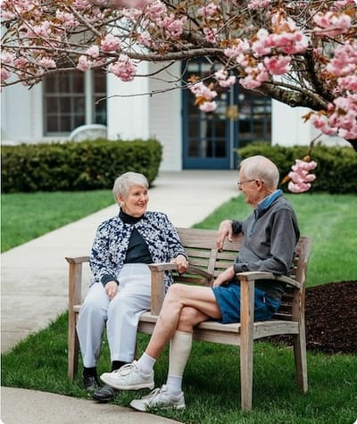 Two residents chatting on a bench under cherry blossoms