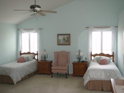 Brightly lit private bedroom with two beds and a chair