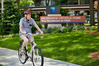 Resident biking in front of Milwaukee Catholic Home